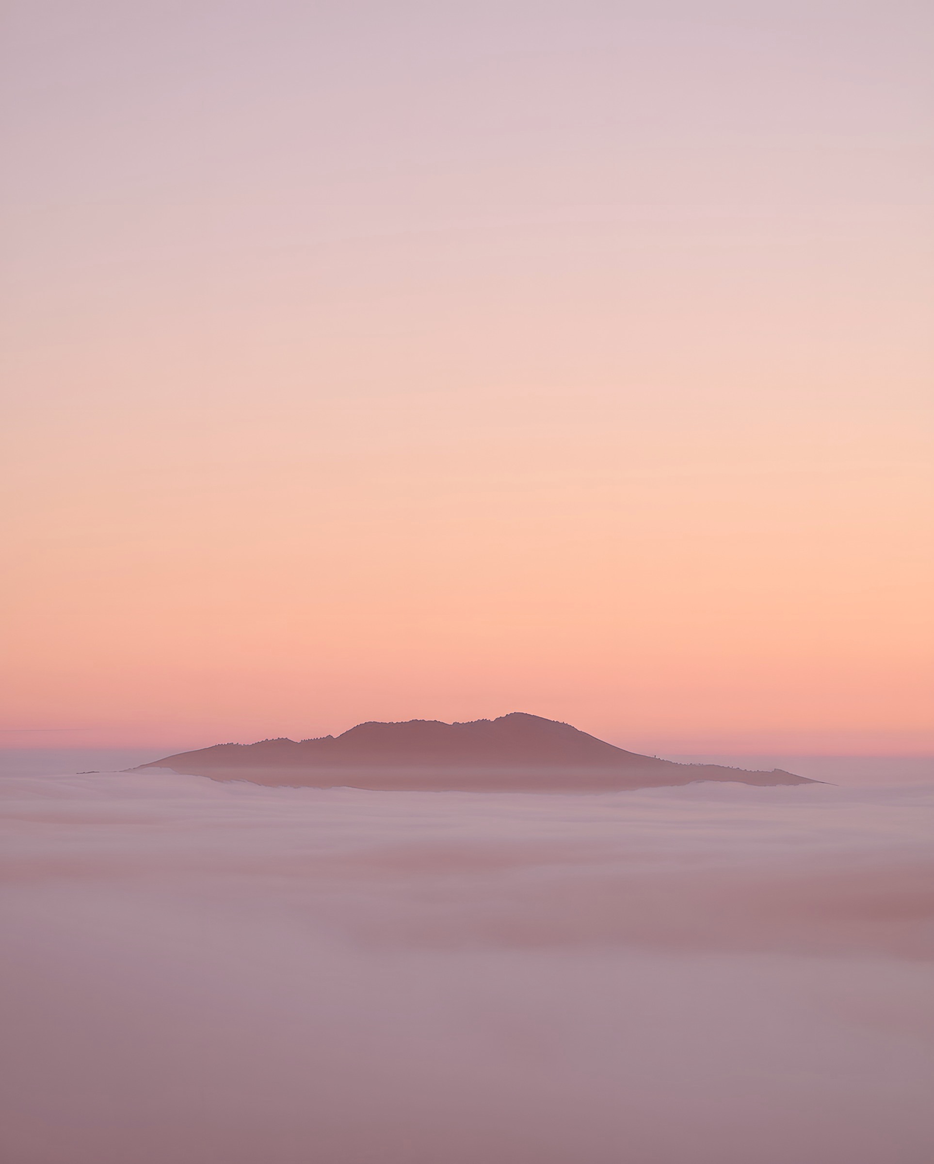 Île sombre émergeant d'une mer de nuages au crépuscule